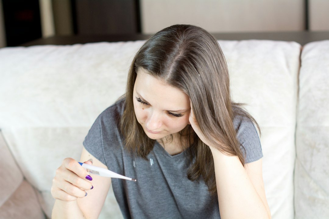 A woman resting at home and checking a thermometer; illustrative photograph
